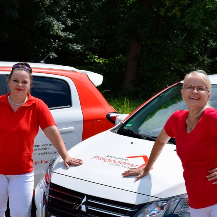 Unsere Mitarbeiter Zwei Frauen in roten T-Shirts stehen vor zwei weißen Autos mit Logo des Pflegedienstes.